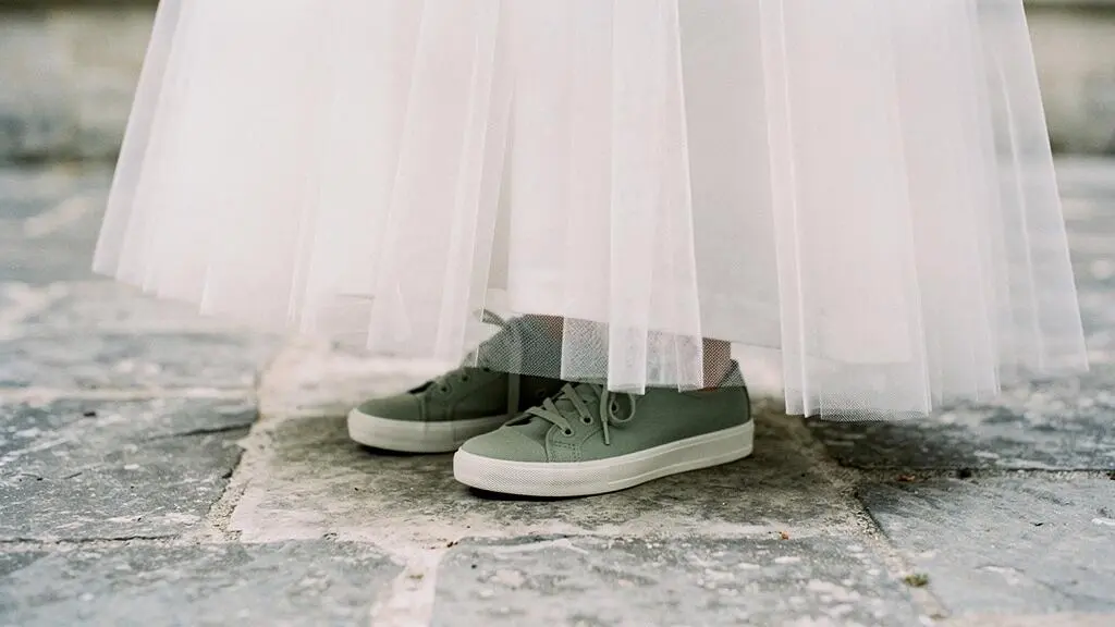 Détail rapproché d'une robe de mariée en tulle avec des baskets vert sauge sur un sol en pierre naturelle